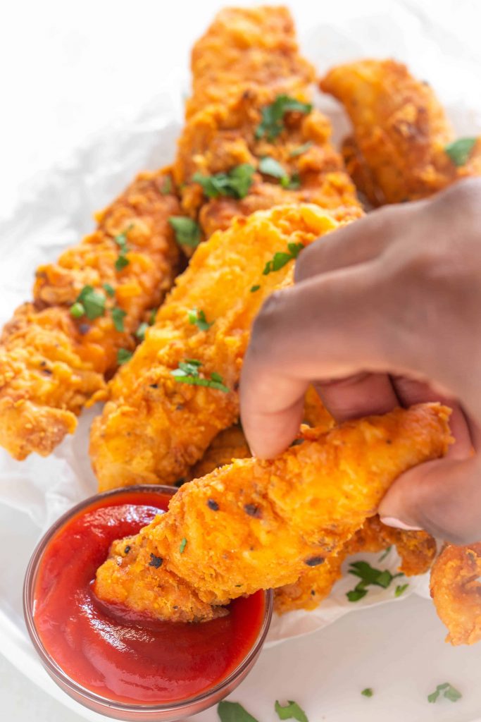 crispy air fryer chicken tenders being dipped into tomato ketchup